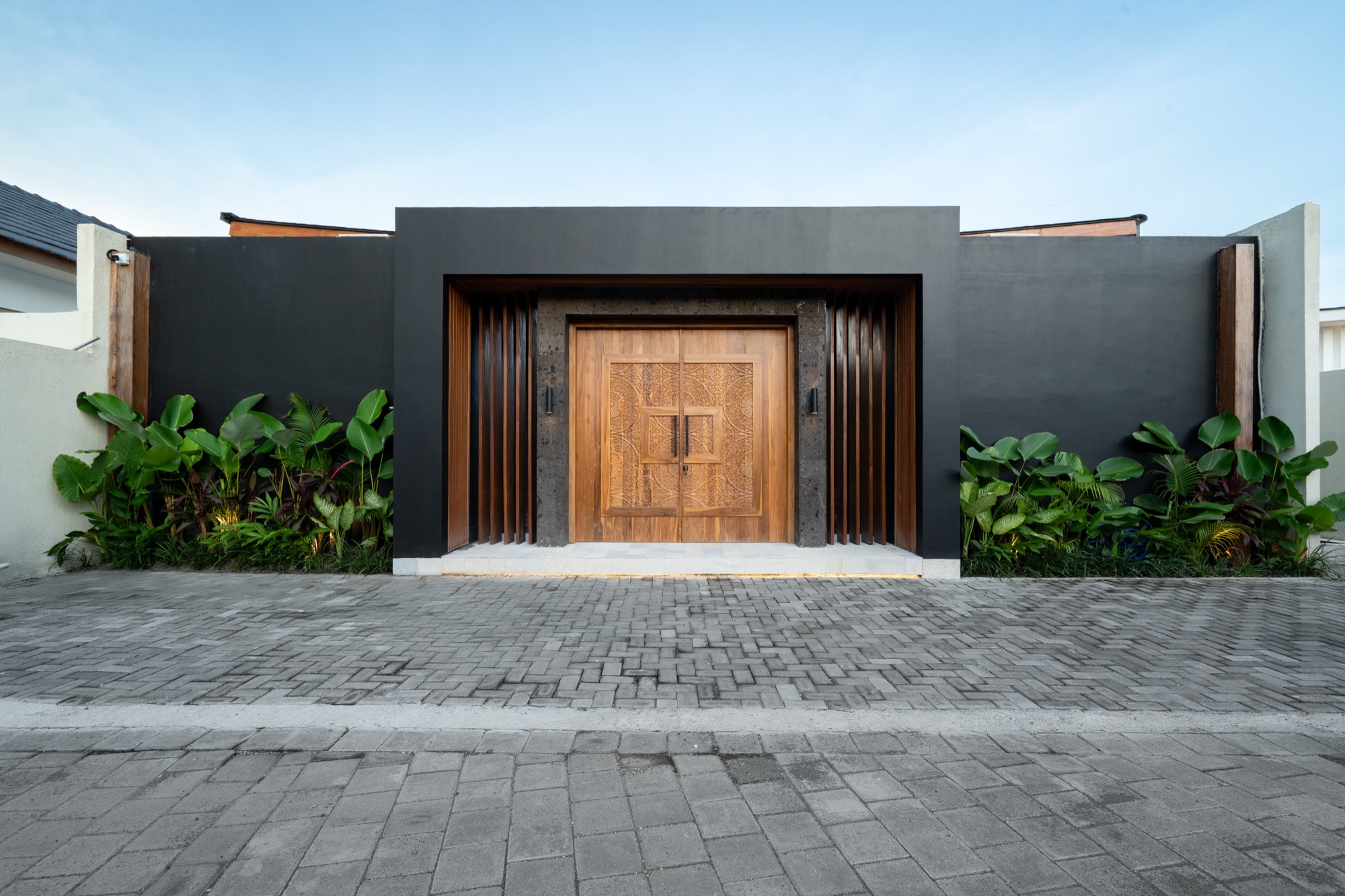 Entrée principale de Villa Beltza — façade noire et double porte sculptée en teck balinais